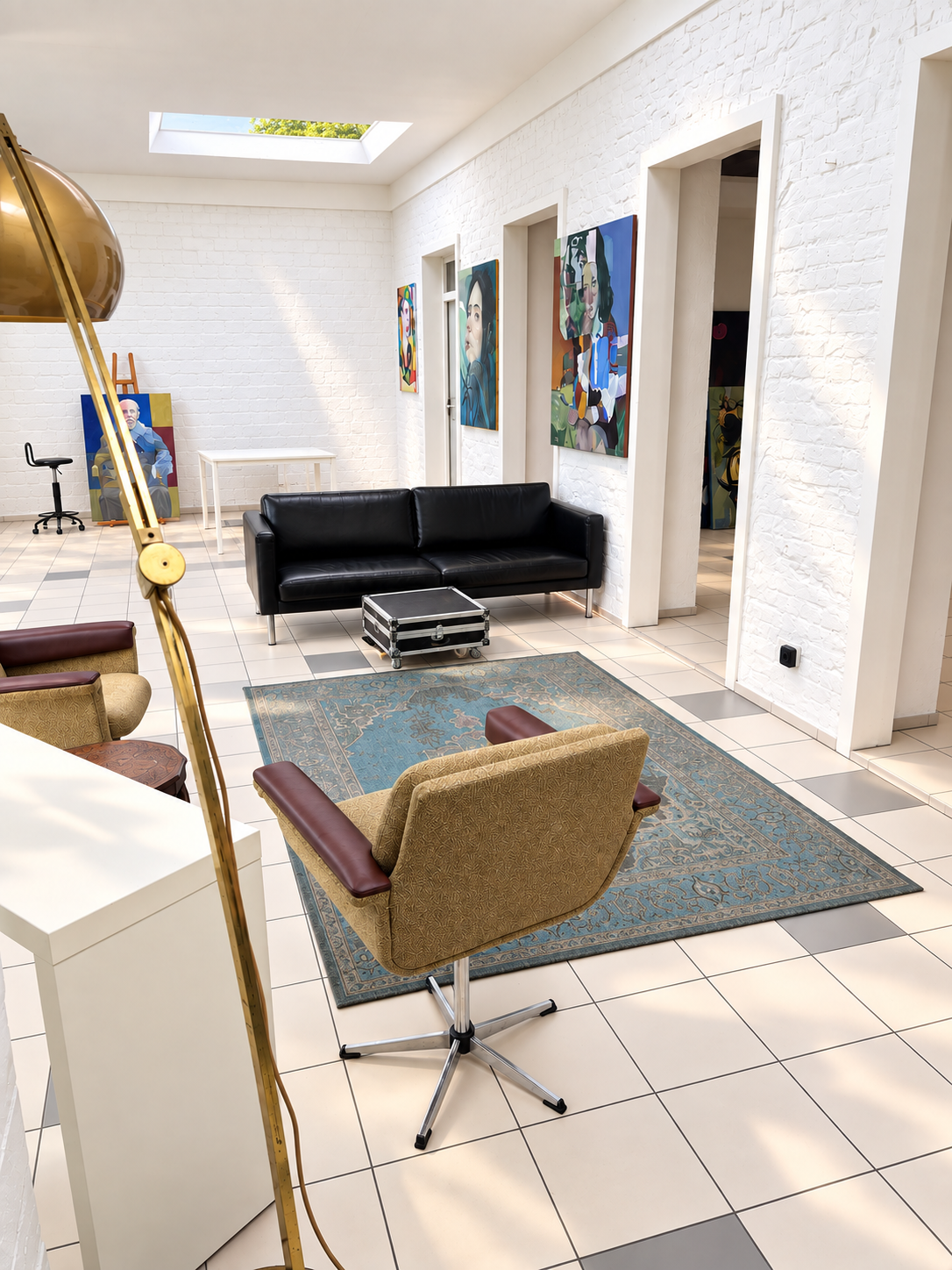 Sitzgruppe mit Sofa, Sesseln und Teppich vor bunten Gemälden im Atelier